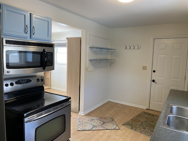 kitchen featuring light wood finished floors, open shelves, appliances with stainless steel finishes, a sink, and blue cabinets