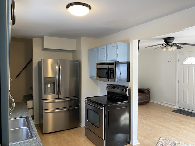 kitchen featuring light wood-style flooring, appliances with stainless steel finishes, a ceiling fan, blue cabinets, and baseboards