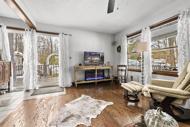 living area with a textured ceiling, ceiling fan, a glass covered fireplace, and wood finished floors