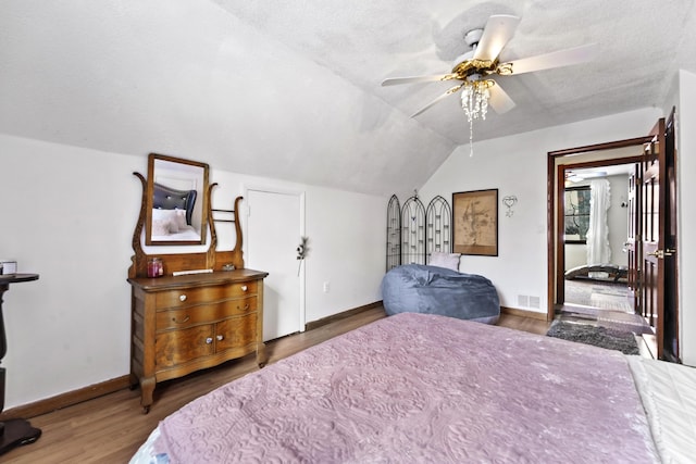 bedroom with lofted ceiling, a textured ceiling, wood finished floors, visible vents, and baseboards