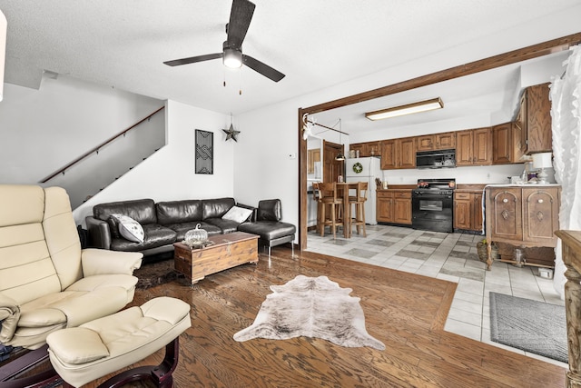 living area with stairs, a textured ceiling, and a ceiling fan