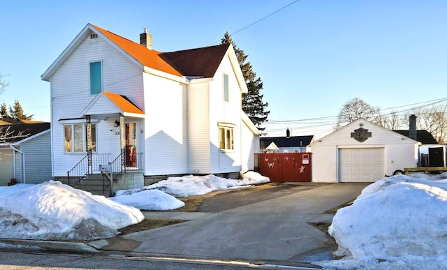 view of front of property featuring driveway, a detached garage, a chimney, an outbuilding, and fence