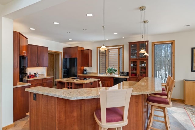 kitchen with a breakfast bar, light stone countertops, a large island with sink, black appliances, and recessed lighting