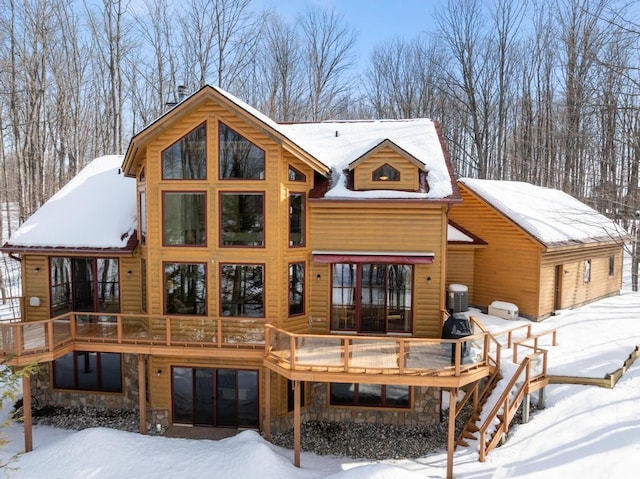 snow covered house featuring stone siding, a wooden deck, and central AC unit