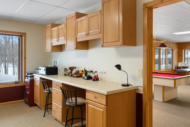 kitchen featuring billiards, light colored carpet, light countertops, a paneled ceiling, and built in desk