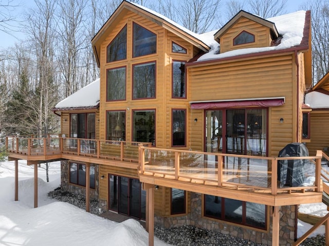 snow covered property with stone siding and a wooden deck