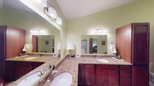 ensuite bathroom with lofted ceiling, double vanity, and a sink