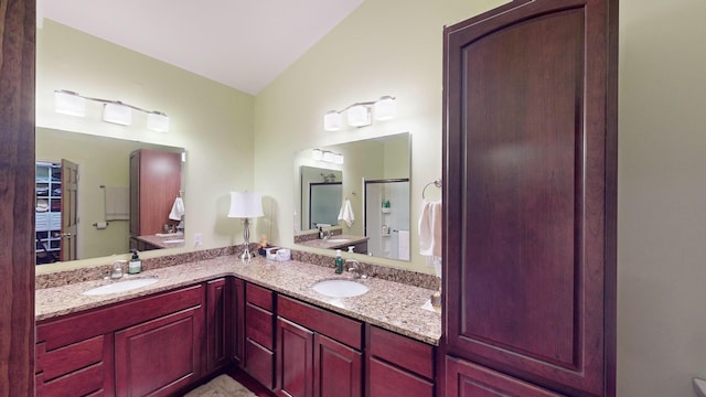 full bathroom with double vanity, a shower with shower door, a sink, and lofted ceiling