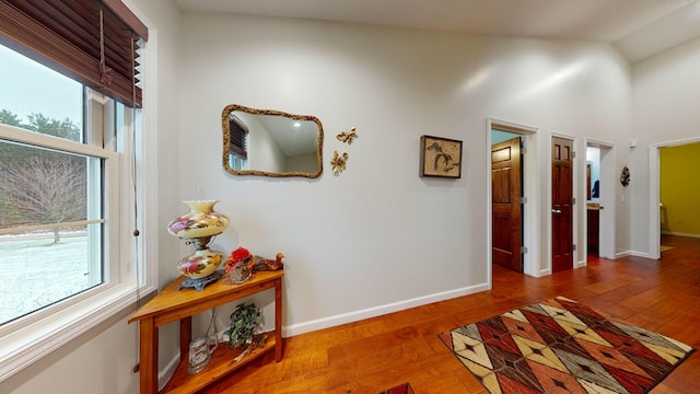 hallway featuring lofted ceiling, baseboards, and wood finished floors