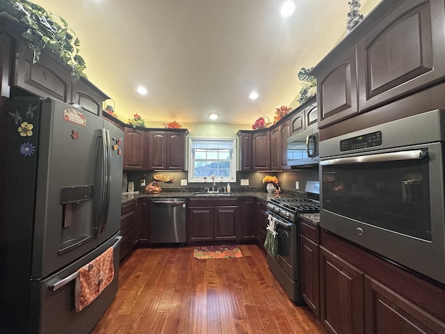 kitchen featuring stainless steel appliances, dark brown cabinets, dark wood-style flooring, and a sink