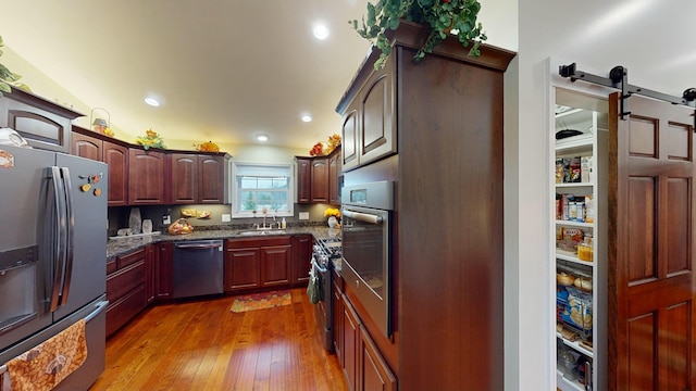 kitchen featuring a barn door, appliances with stainless steel finishes, hardwood / wood-style floors, dark stone countertops, and a sink