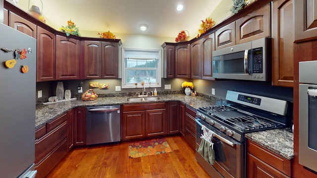 kitchen with recessed lighting, stainless steel appliances, wood finished floors, a sink, and dark stone counters