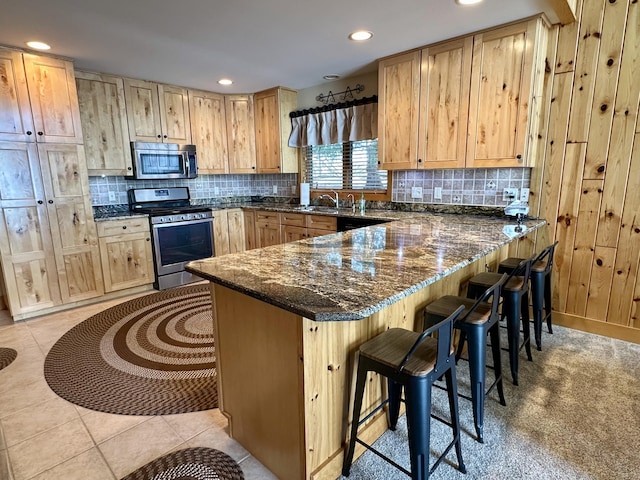 kitchen with light brown cabinets, stainless steel appliances, a peninsula, and backsplash