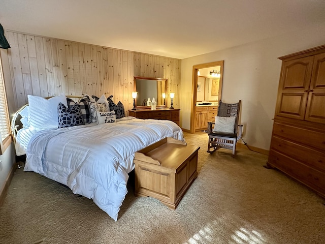 bedroom featuring light colored carpet, wood walls, baseboards, and ensuite bathroom