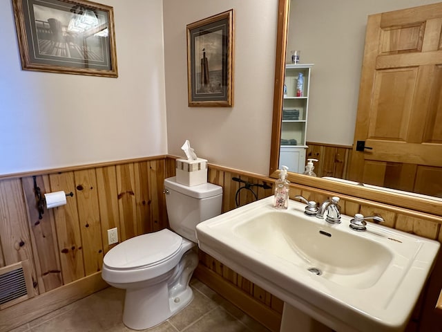 bathroom with toilet, a sink, visible vents, wainscoting, and tile patterned floors