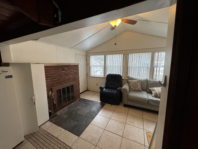 living area with a fireplace, vaulted ceiling, a ceiling fan, and tile patterned floors