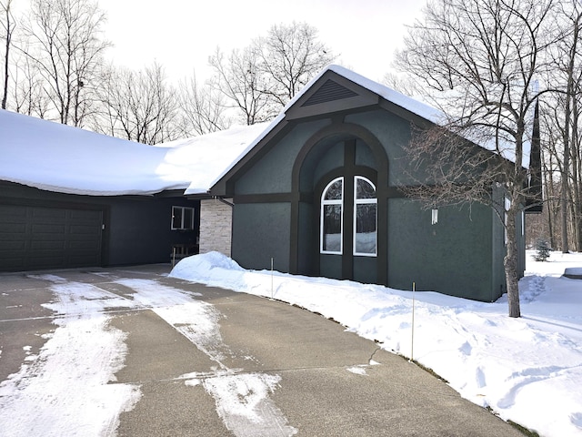 view of front facade featuring driveway, stone siding, and stucco siding