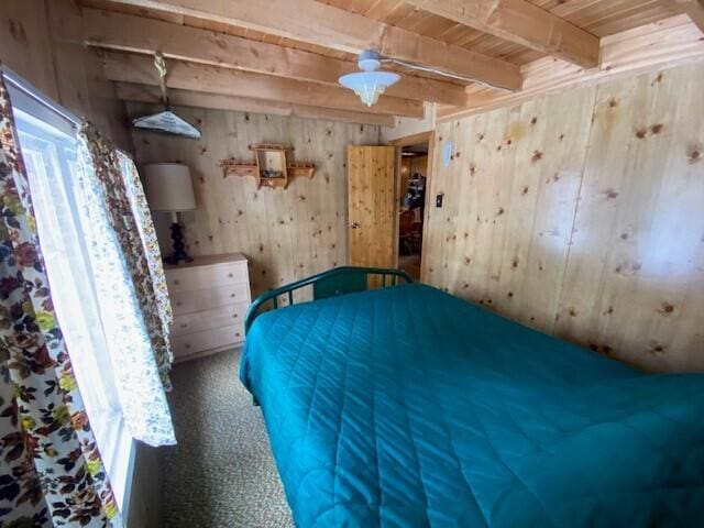 unfurnished bedroom with wooden ceiling, carpet, wooden walls, and beamed ceiling