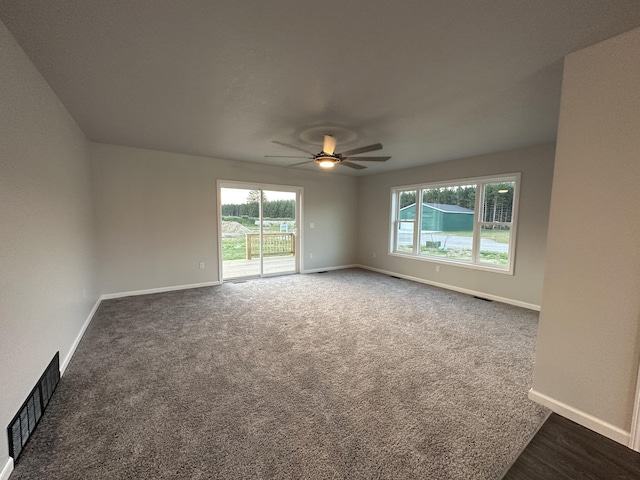 empty room featuring dark carpet, visible vents, ceiling fan, and baseboards