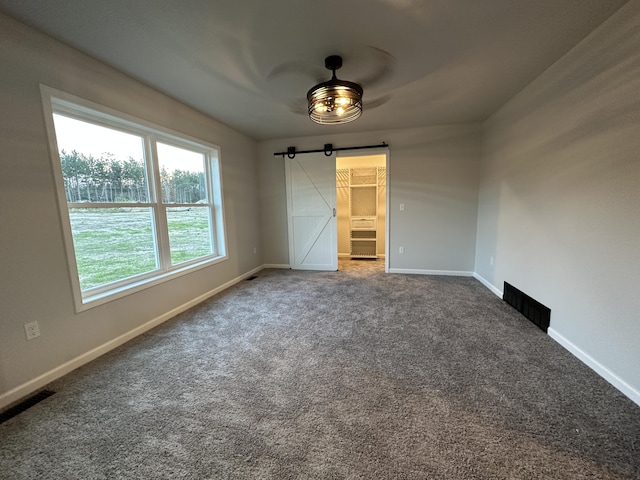 carpeted empty room featuring visible vents, baseboards, and a barn door