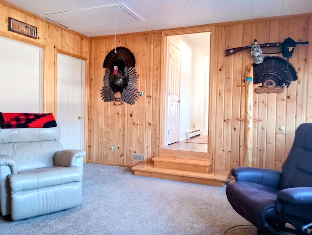 living area with a baseboard heating unit, attic access, carpet flooring, and wooden walls