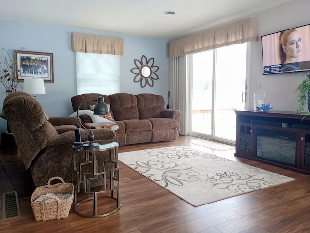 living area featuring visible vents, wood finished floors, and a glass covered fireplace