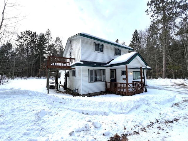 snow covered back of property featuring stairway and a deck