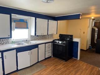 kitchen featuring decorative backsplash, wood finished floors, light countertops, a sink, and gas stove