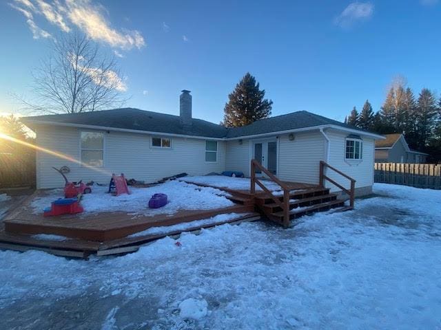 snow covered back of property with french doors, a chimney, a deck, and fence