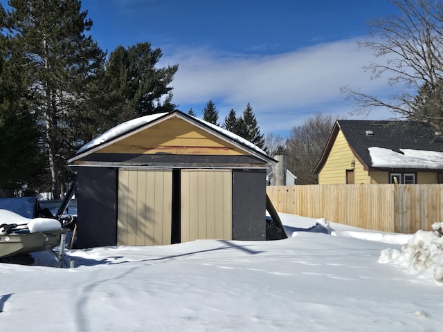 snow covered structure with an outbuilding and fence