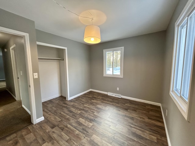 unfurnished bedroom featuring dark wood-style floors, a closet, visible vents, and baseboards