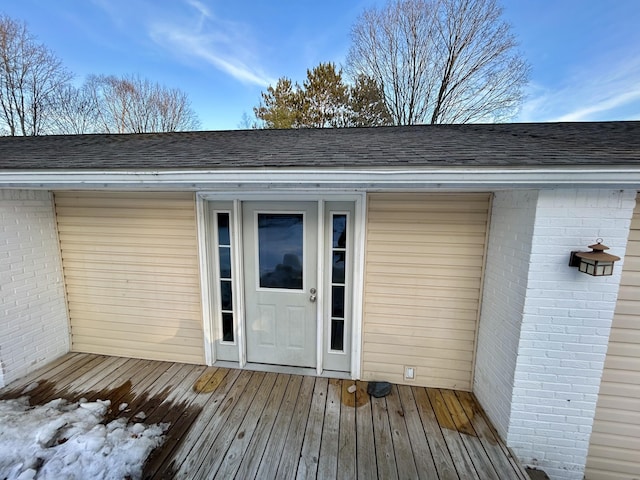 doorway to property featuring a shingled roof and brick siding