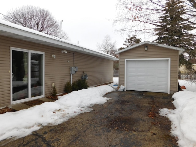 view of snowy exterior featuring an outbuilding, driveway, and a detached garage