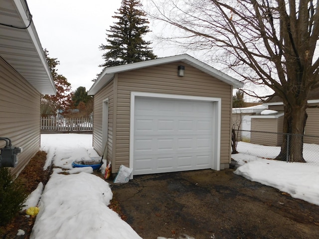 snow covered garage featuring a garage and fence