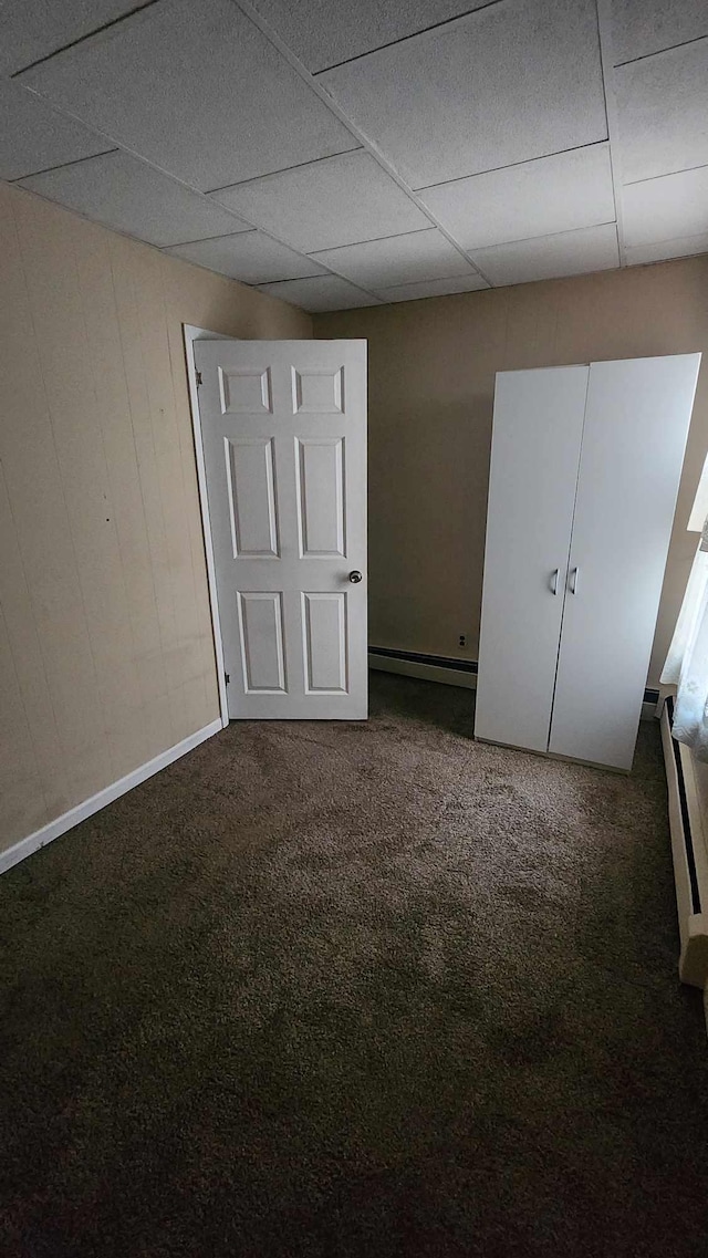 unfurnished bedroom featuring baseboard heating, baseboards, a drop ceiling, and carpet flooring