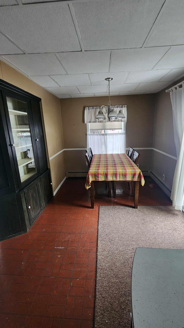 dining area featuring brick floor, a baseboard radiator, a drop ceiling, and baseboards