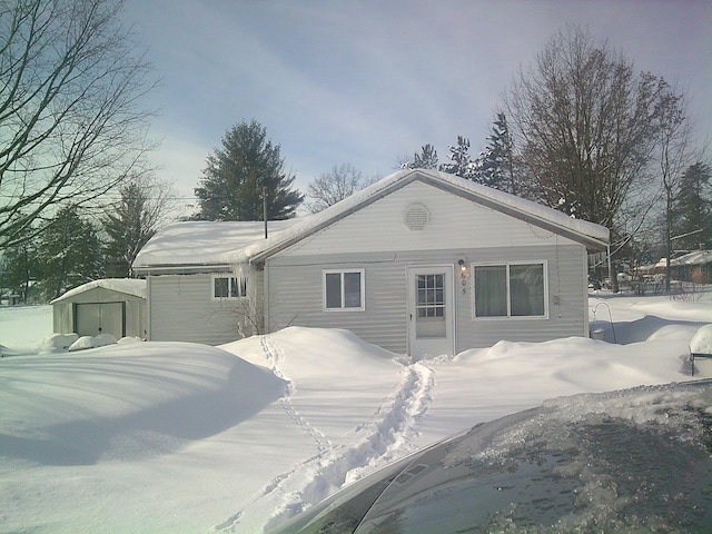 snow covered back of property featuring an outdoor structure