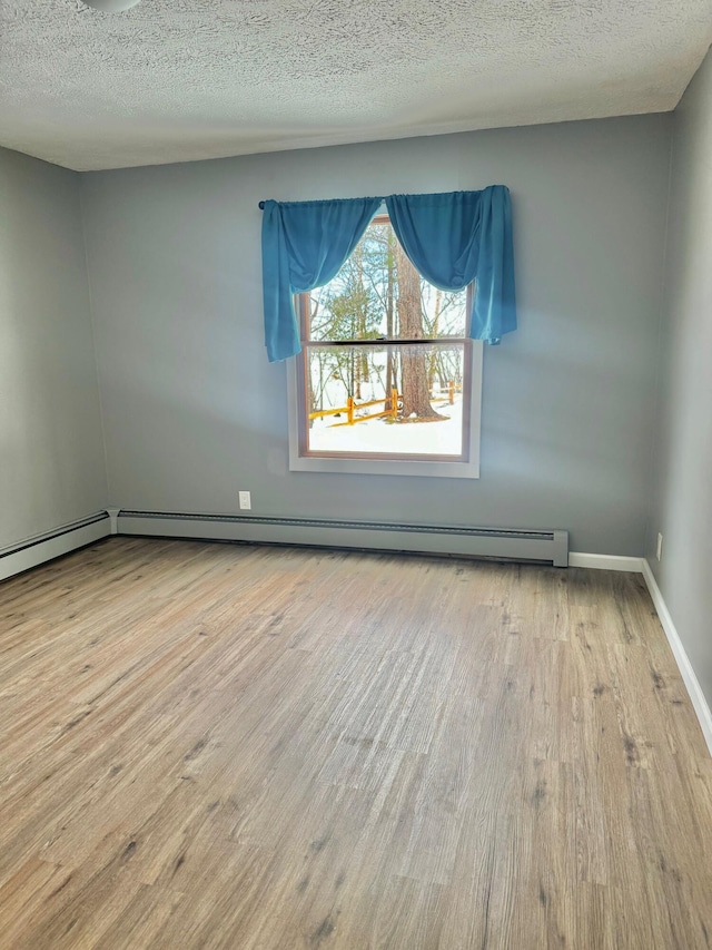 spare room with a baseboard heating unit, a textured ceiling, baseboards, and wood finished floors