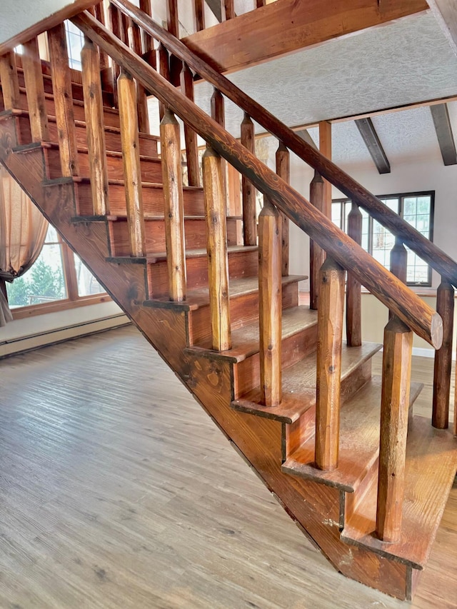 stairway with beamed ceiling, plenty of natural light, and wood finished floors