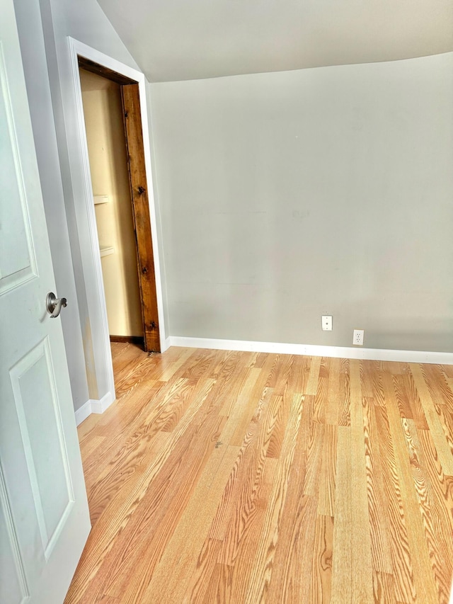 spare room featuring lofted ceiling, light wood-type flooring, and baseboards