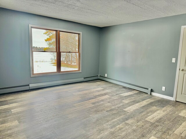 spare room featuring a textured ceiling, baseboard heating, wood finished floors, and baseboards