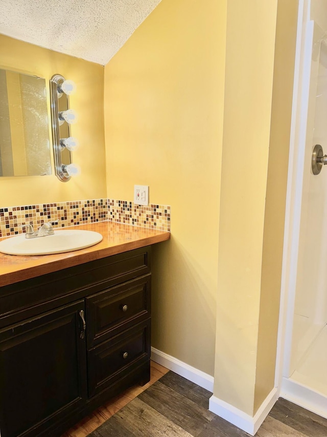 bathroom featuring walk in shower, wood finished floors, vanity, and decorative backsplash