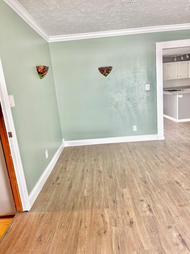 empty room with a textured ceiling, ornamental molding, wood finished floors, and baseboards