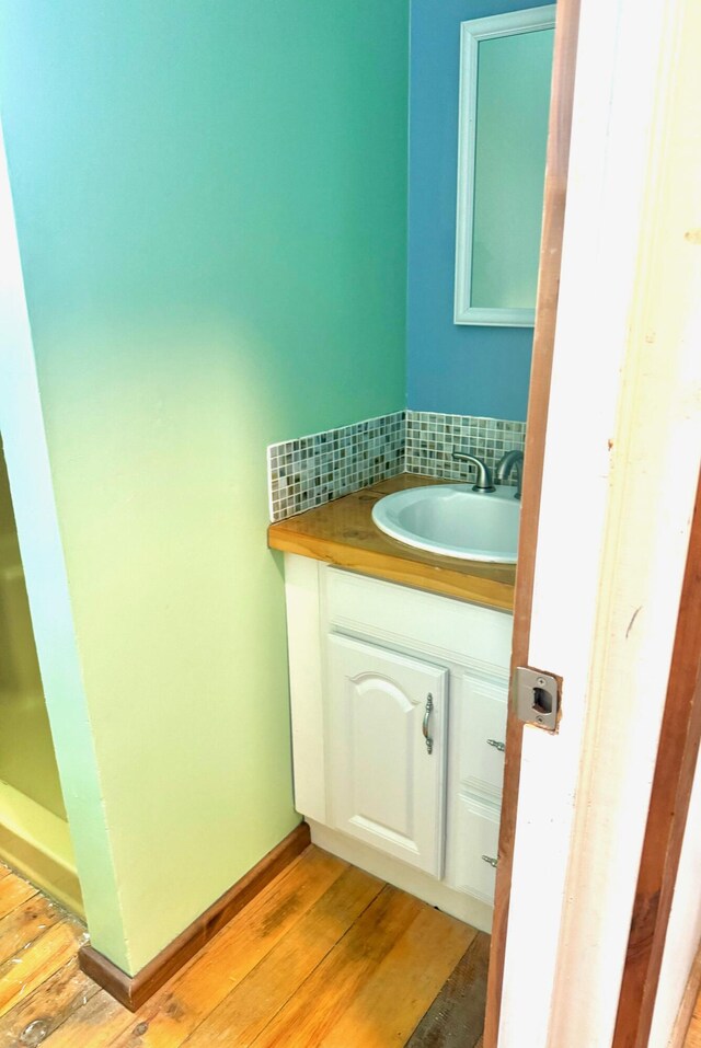 bathroom featuring baseboards, decorative backsplash, wood finished floors, and vanity