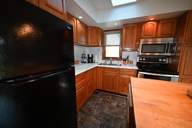 kitchen featuring a skylight, appliances with stainless steel finishes, brown cabinets, wooden counters, and a sink