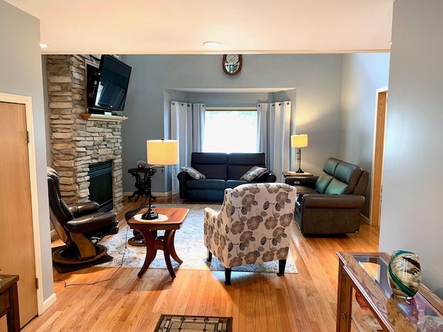 living area with light wood-style floors, a stone fireplace, and baseboards