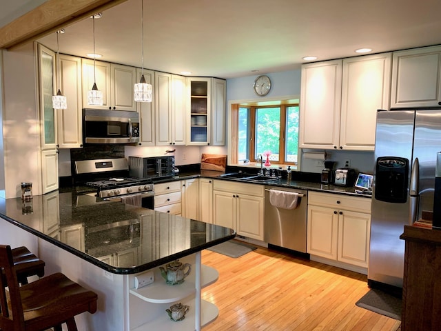 kitchen with a breakfast bar area, open shelves, stainless steel appliances, a sink, and a peninsula