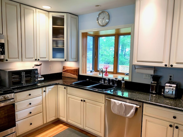 kitchen with a toaster, appliances with stainless steel finishes, glass insert cabinets, a sink, and dark stone counters