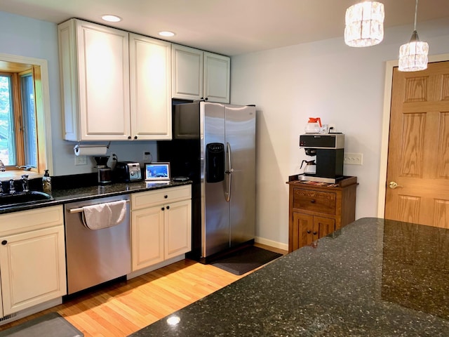 kitchen featuring stainless steel appliances, a sink, light wood finished floors, dark stone countertops, and pendant lighting