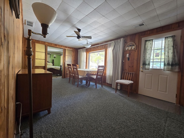 dining area with visible vents, ceiling fan, wooden walls, and carpet flooring